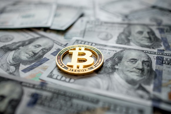 Eine symbolische Bitcoin-Münze liegt auf 100-Dollar-Banknoten.