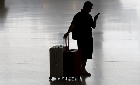 epa12931624 A traveler with luggage looks at a mobile phone after arriving at the international arrivals terminal in Suvarnabhumi Airport in Samut Prakan province, on the outskirts of Bangkok, Thailan ...