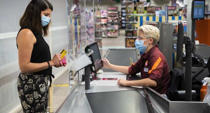 Une personne paie des courses a la caisse a une vendeuse portant un masque sur le visage dans un magasin Migros le mercredi 8 juillet 2020 a Crissier. Les masques sont obligatoires dans les magasins d ...