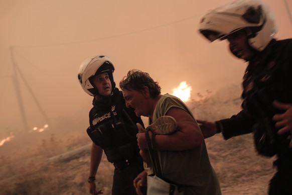epa10813697 Police officers evacuate an elderly lady during a wildfire at the area of Fyli near Athens, Greece, 22 August 2023. A wildfire is in progress in Fyli, west Attica region. So far, 26 firefi ...