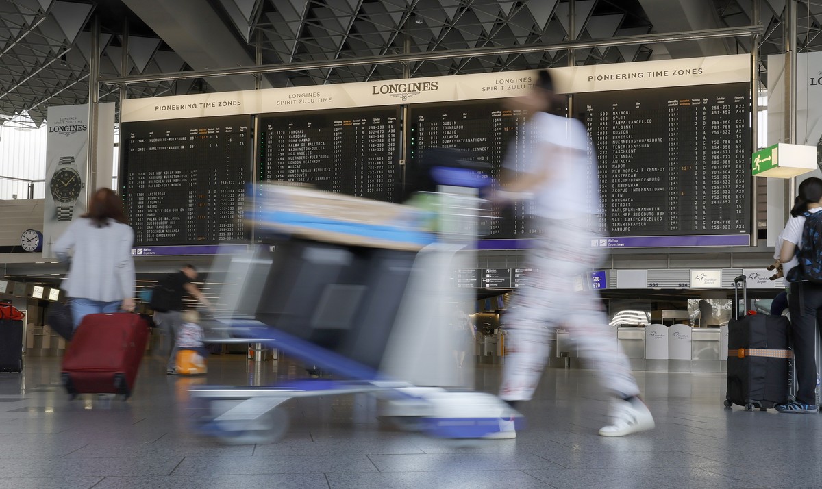 epa10761661 Passengers with their luggage move in a terminal building with a flight information board at the international airport in Frankfurt am Main, Germany, 22 July 2023. Summer vacations began i ...