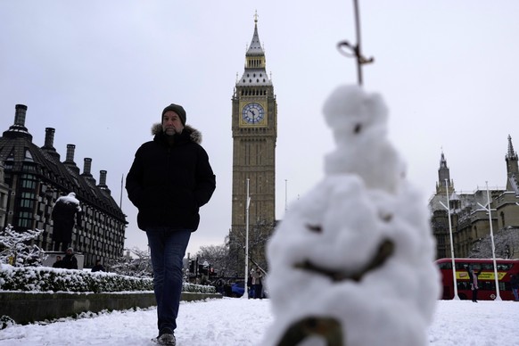 A man walks past a snowman in London, Monday, Dec. 12, 2022. Snow and ice have swept across parts of the UK, with cold wintry conditions set to continue for days. (AP Photo/Kin Cheung)