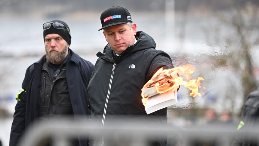 epa10420408 Leader of the far-right Danish political party Stram Kurs, Rasmus Paludan, burns a copy of the Kuran, while being watched by police officers, as he protests outside the Turkish embassy in  ...