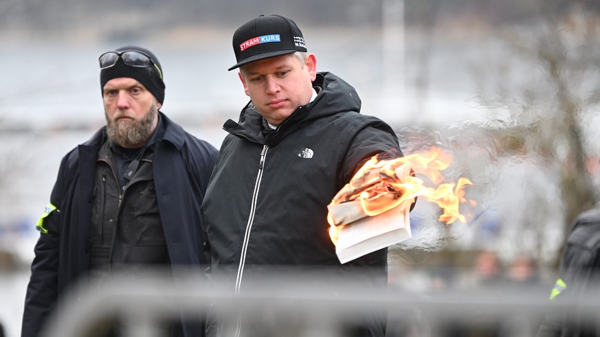 epa10420408 Leader of the far-right Danish political party Stram Kurs, Rasmus Paludan, burns a copy of the Kuran while being watched by police officers, as he protests outside the Turkish embassy in…