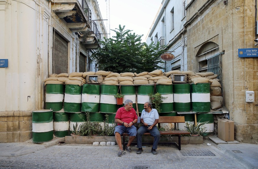 epa06051378 Two men sit on a bench next to a barricade outside the UN buffer zone, also known as the &#039;Green Line&#039; in the ethnically-divided capital city of Nicosia, Cyprus, 26 June 2017. Riv ...