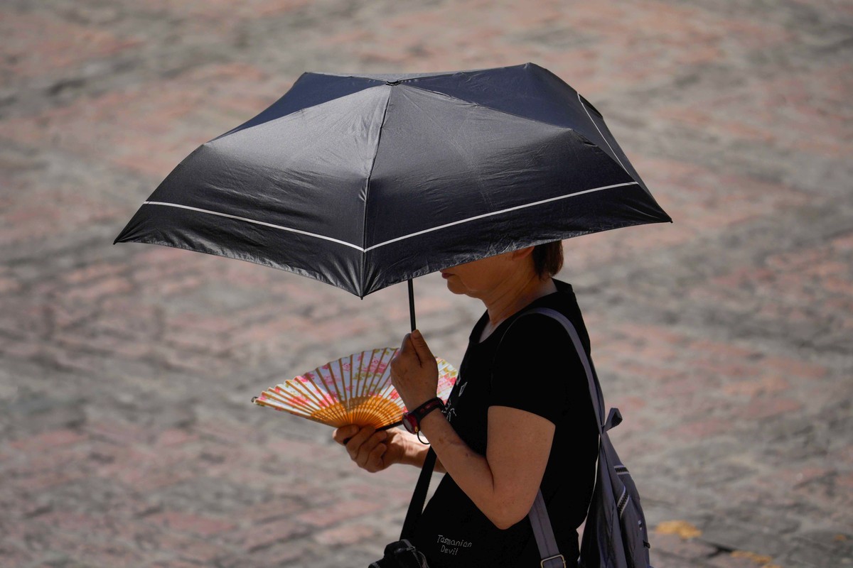 epa10710665 A woman uses a fan and protects herself from the sun with an umbrella in Cordoba, Spain, 25 June 2023. The current anticyclonic situation in Spain has led to the first heat wave of the sum ...