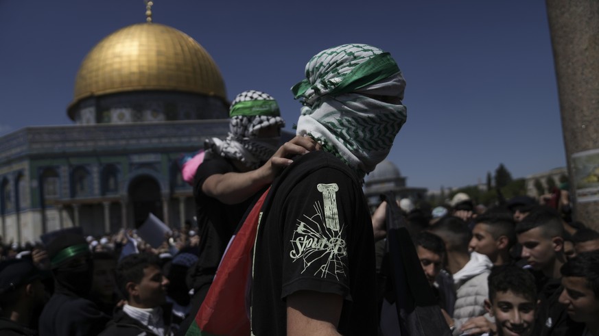 Masked Palestinians carry their national flag and wear headbands in support of Hamas&#039; military wing, the Qassam Brigades in a protest against Israel, after midday prayers next to the Dome of Rock ...