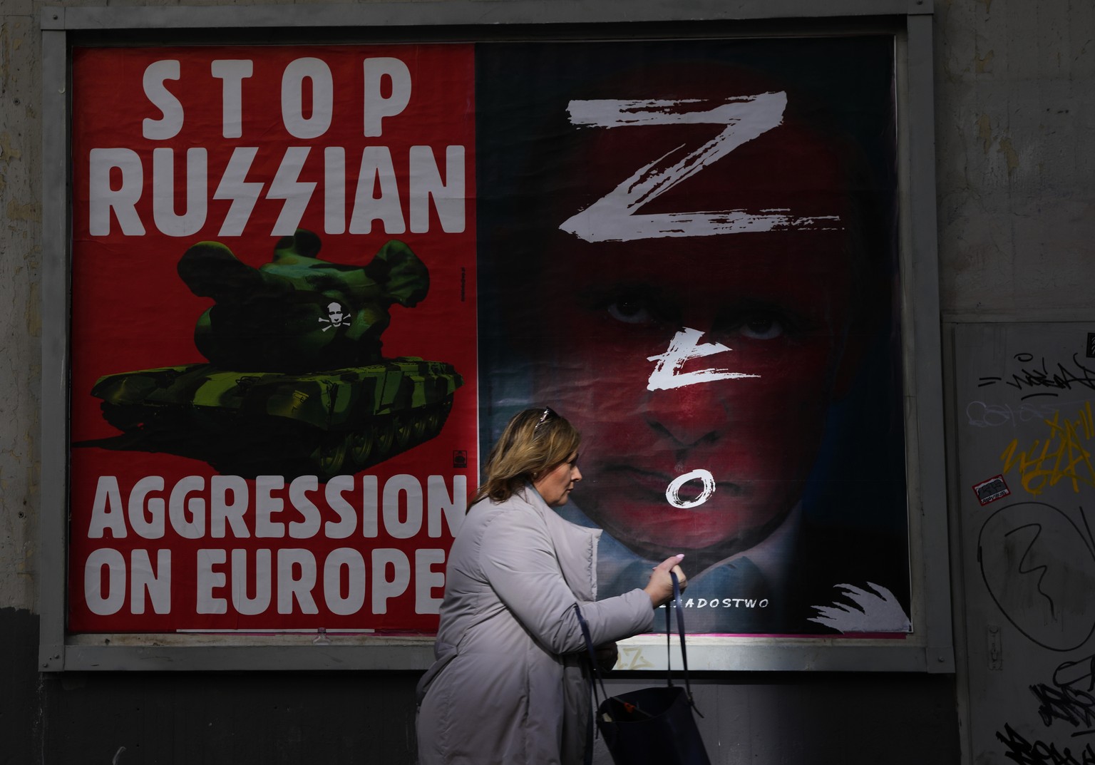 A woman walks past a wall with posters depicting Russian President Vladimir Putin, right, in Warsaw, Poland, on Thursday, March 24, 2022. Ukraine President Volodymr Zelenskyy called on people worldwid ...