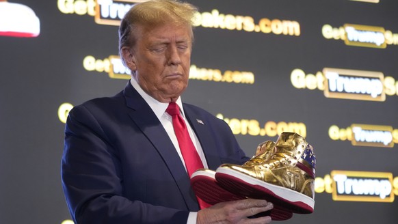 Republican presidential candidate former President Donald Trump holds gold Trump sneakers at Sneaker Con Philadelphia, an event popular among sneaker collectors, in Philadelphia, Saturday, Feb. 17, 20 ...