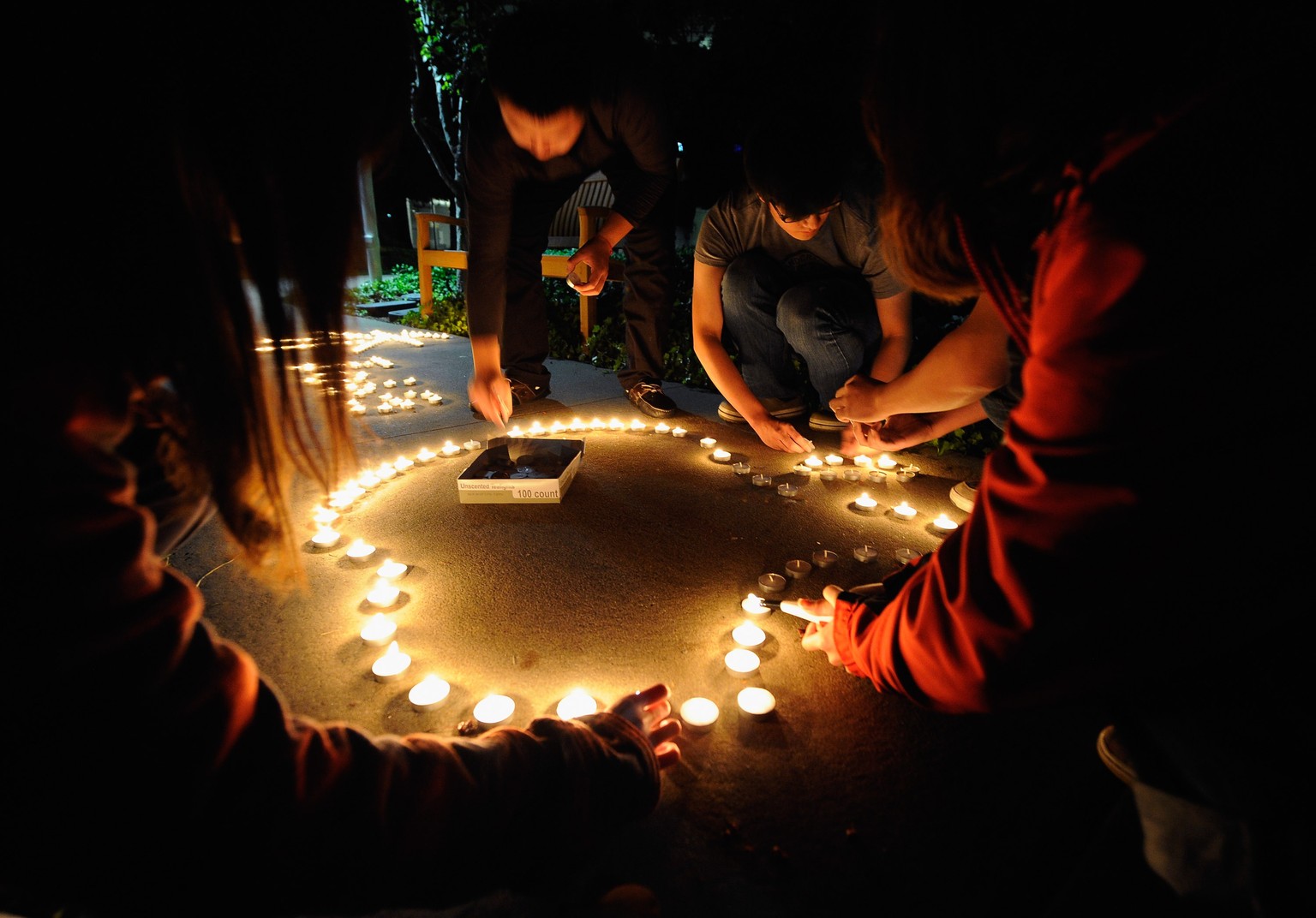 CUPERTINO, CA - OCTOBER 05: Chinese exchange students from nearby De Anza College use candles to create the Apple logo and Steve Jobs&#039; last name in Chinese characters at a makeshift memorial for  ...