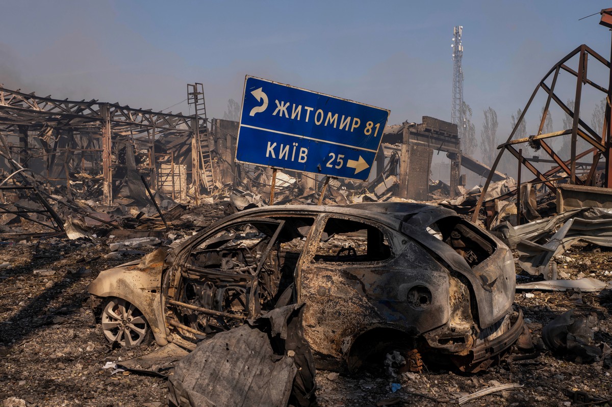 A view of a destroyed car stands amid damaged buildings, with a road sign showing the direction and distance to Kyiv and Zhytomyr after a Russian attack struck a warehouse, followed by an explosion, i ...