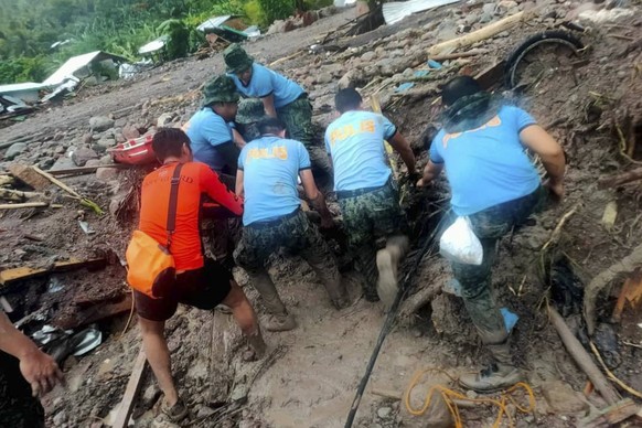 In this handout photo provided by the Philippine Coast Guard, rescuers retrieve bodies during the search and rescue operations due to landslides caused by Tropical Storm Nalgae in Barangay Kushong, Da ...