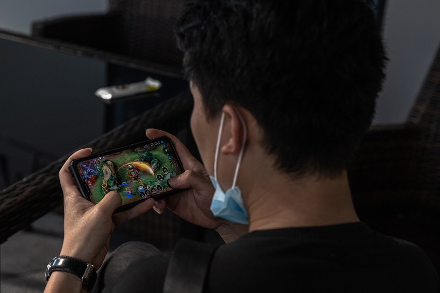 epa09429687 A man plays Honor of Kings game on his mobile phone in the shopping and residential area of Sanlitun, in Beijing, China, 25 August 2021 (issued 26 August 2021). Online games in China are e ...