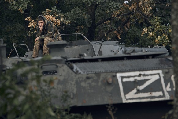 Ein ukrainischer Soldat sitzt auf einem zerstörten russischen Panzer.