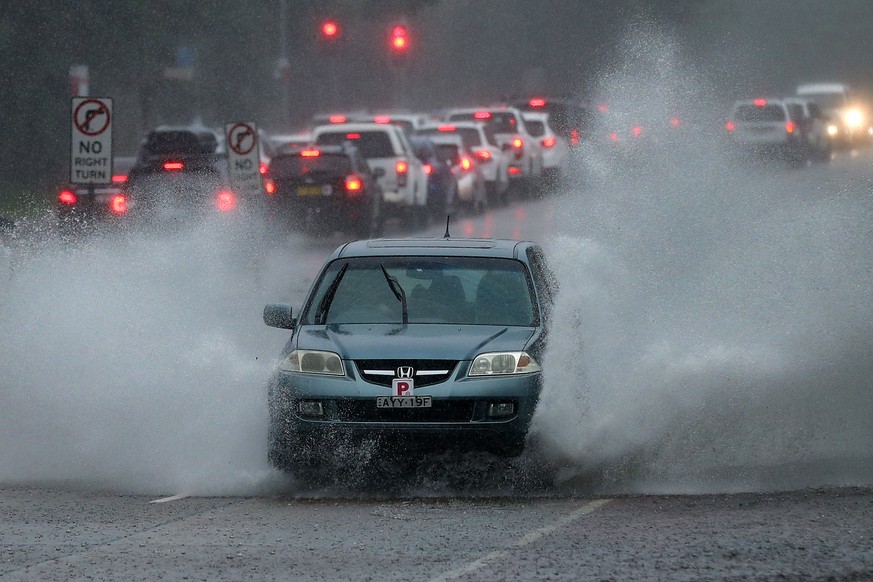 epa09085408 A car drives through a pool of standing water on the Northern Beaches in Sydney, Australia, 20 March 2021. More rain is forecast for the New South Wales coast and other parts of the state, ...