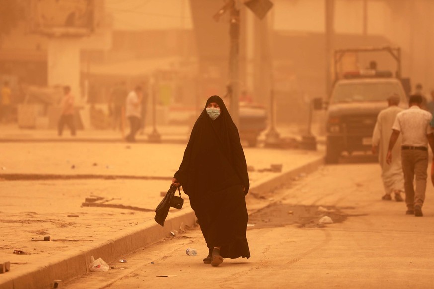 epaselect epa09951007 An Iraqi woman wears a face mask and walks at a street shrouded in heavy dust in central Baghdad, Iraq, 16 May 2022. The dust storm sent thousends of people with respiratory prob ...