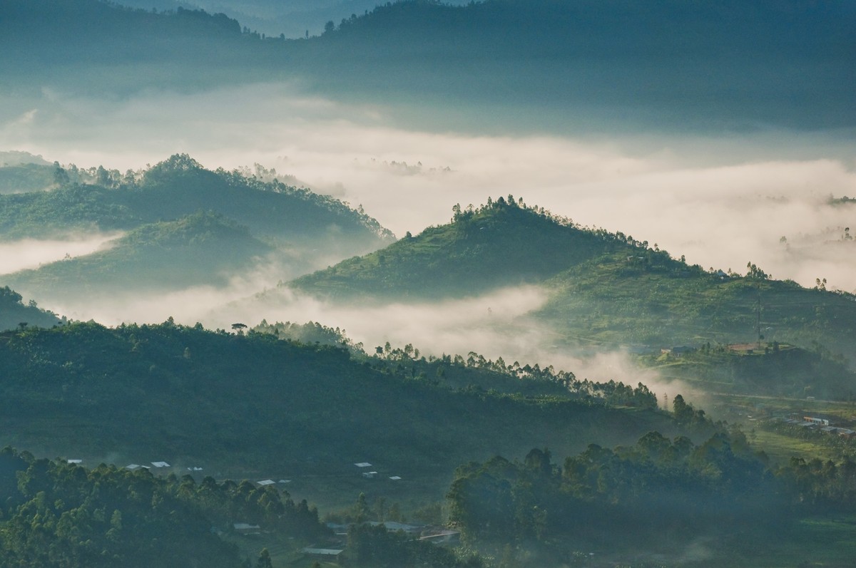 Houses in a small village are dwarfed by the looming presence of a volcanic mountain, Rwanda,