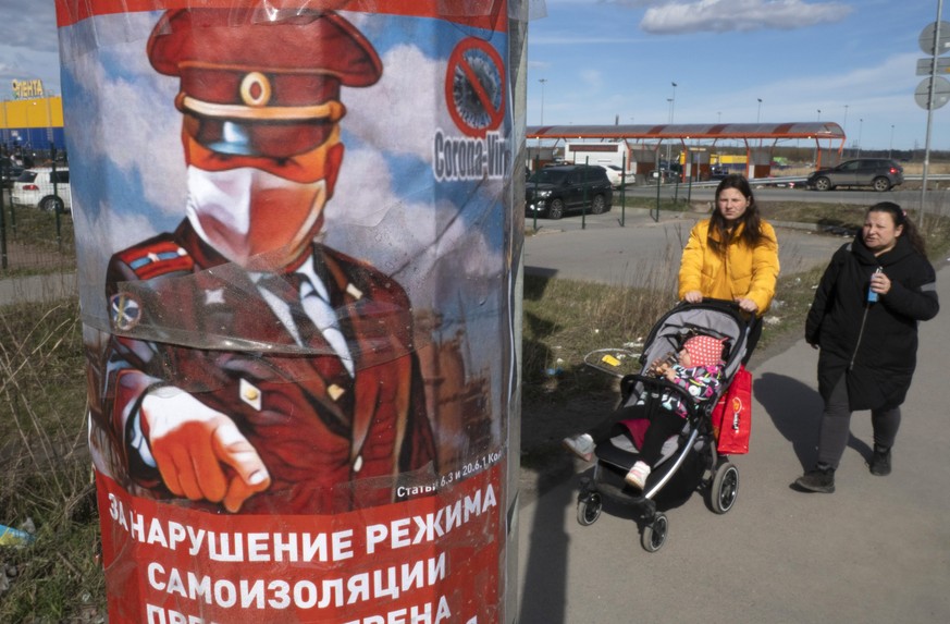 Women walk past a poster depicting a policeman warning of liability for violation of self-isolation regime, according to the order of the city authorities due to the coronavirus in St.Petersburg, Russ ...