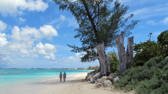 FILE - In this Aug. 3, 2012 file photo, tourists walk along the shore of Seven Mile Beach in Grand Cayman Island. The Caribbean boasts two new shark sanctuaries as the Cayman Islands and St. Maarten o ...