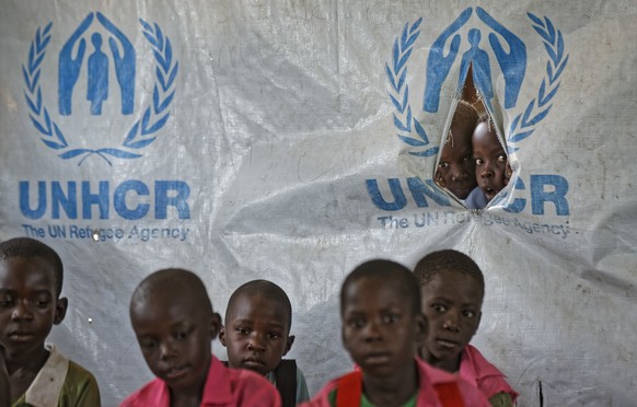 In this photo taken Wednesday, June 7, 2017, children look through a tear in the tarpaulin tents that serve as extra classrooms, for a mixed class of South Sudanese refugee children and Ugandan childr ...
