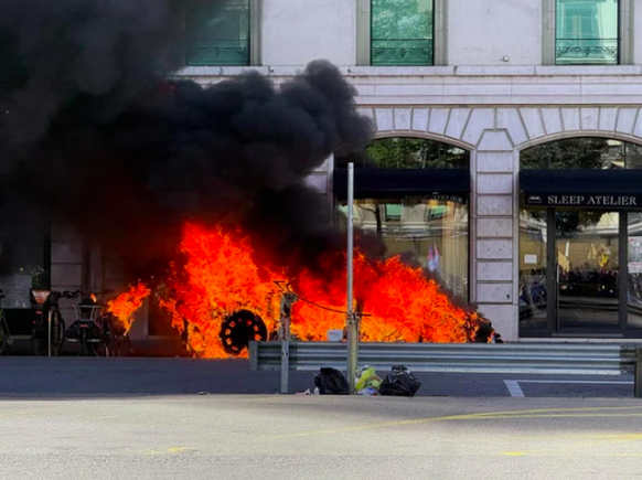 Demonstrierende setzen einen Tesla in Brand.