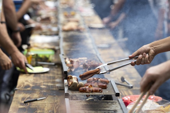 Ein Besucher wendet einen Cervelat auf dem Grill, waehrend der Bundesfeier am Freitag, 1. August 2025 auf dem Bundesplatz in Bern. (KEYSTONE/Peter Klaunzer)