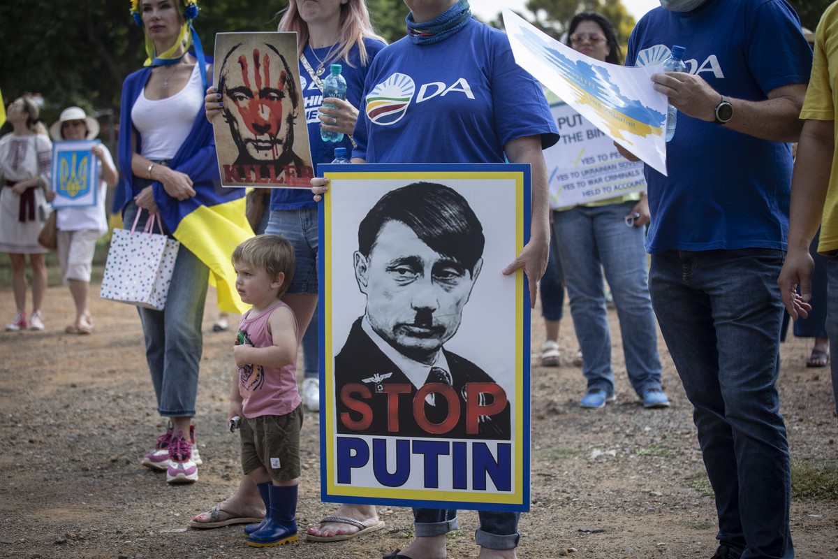 epa09817253 A demonstrator holds a placard depicting a caricature of Russian President Putin as they listen to speeches during a peace rally against Russia's invasion of Ukraine, in Pretoria, Sou ...