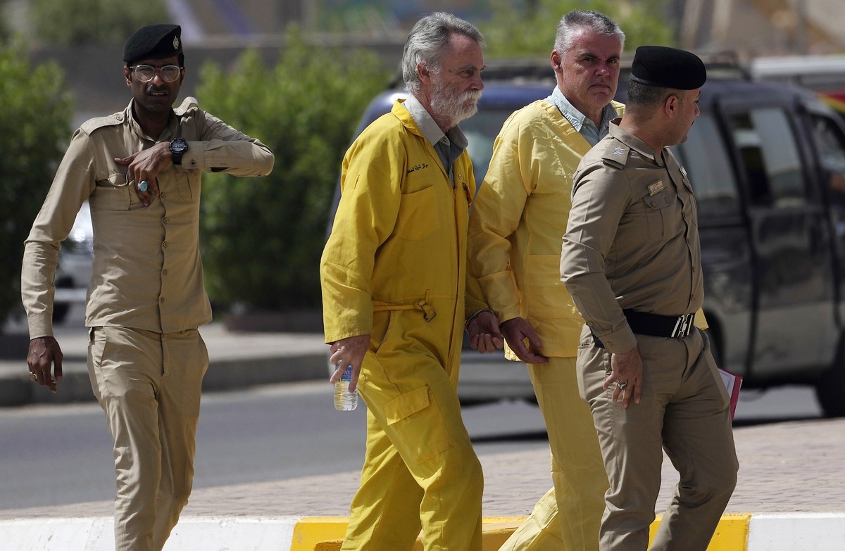 Volker Waldmann, right, and Jim Fitton, center, are handcuffed as they walk to a courtroom escorted by police arriving to court in Baghdad, Iraq, Sunday, May 22, 2022. Waldmann and Fitton have been ac ...