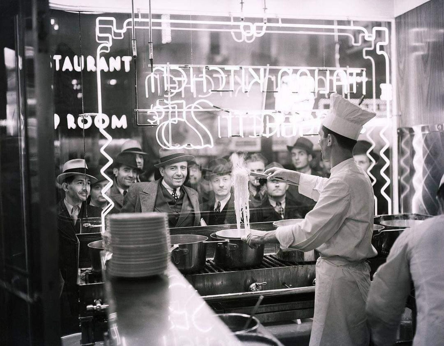 Pedestrians look through a restaurant window to watch a cook prepare a pot of spaghetti in New York City, 1937.