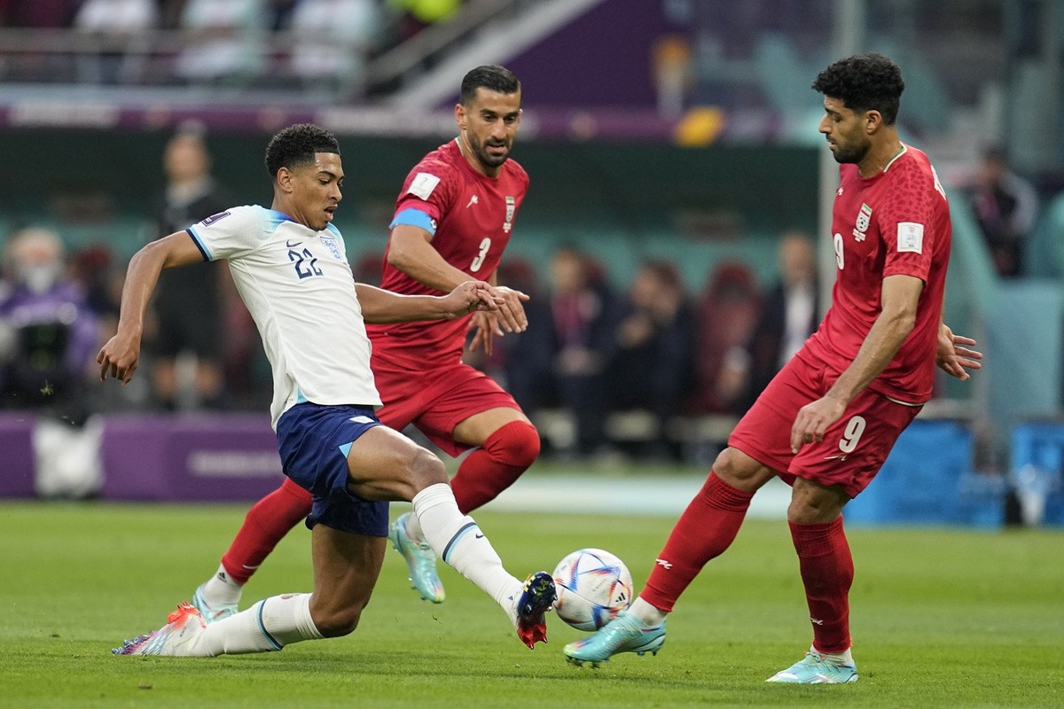 England's Jude Bellingham, left, fights for the ball with Iran's Ehsan Hajsafi, center, and Mehdi Taremi during the World Cup group B soccer match between England and Iran at the Khalifa Int ...