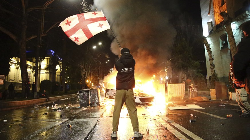 A man waves a Georgian national flag in front of a burning barricade, not far from the Georgian parliament building in Tbilisi, Georgia, Thursday, March 9, 2023. Police in the capital of Georgia used  ...