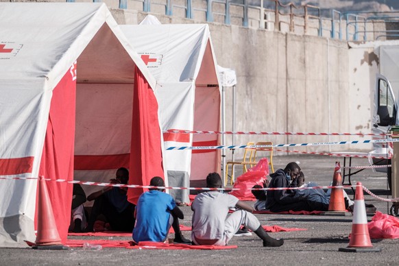 epa08583388 A group of migrants who arrived in the last three days sit at the dock of Arguineguin, Gran Canaria, Canary Islands, Spain, 04 August 2020. Some 71 migrants arrived and they wait to go thr ...