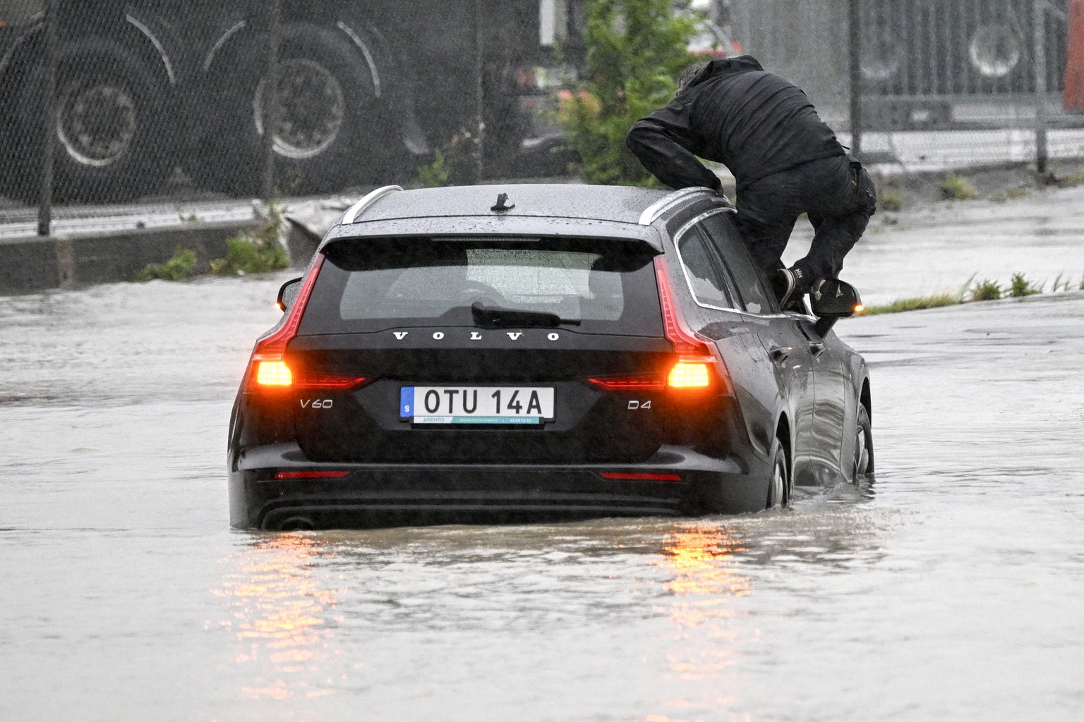 A man climbs out of a car which got stuck at a flooded roundabout in Arl