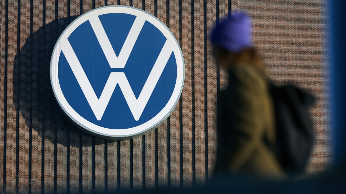 epa11947107 A person walks next to the logo of German car maker Volkswagen (VW) on a wall at the company's plant in Wolfsburg, Germany, 07 March 2025. The company will hold the annual press confe ...