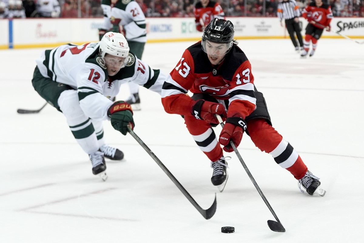 Minnesota Wild left wing Matt Boldy (12), left, and New Jersey Devils center Nico Hischier (13), right, fight for the puck during the third period of an NHL hockey game, Monday, March 31, 2025, in New ...