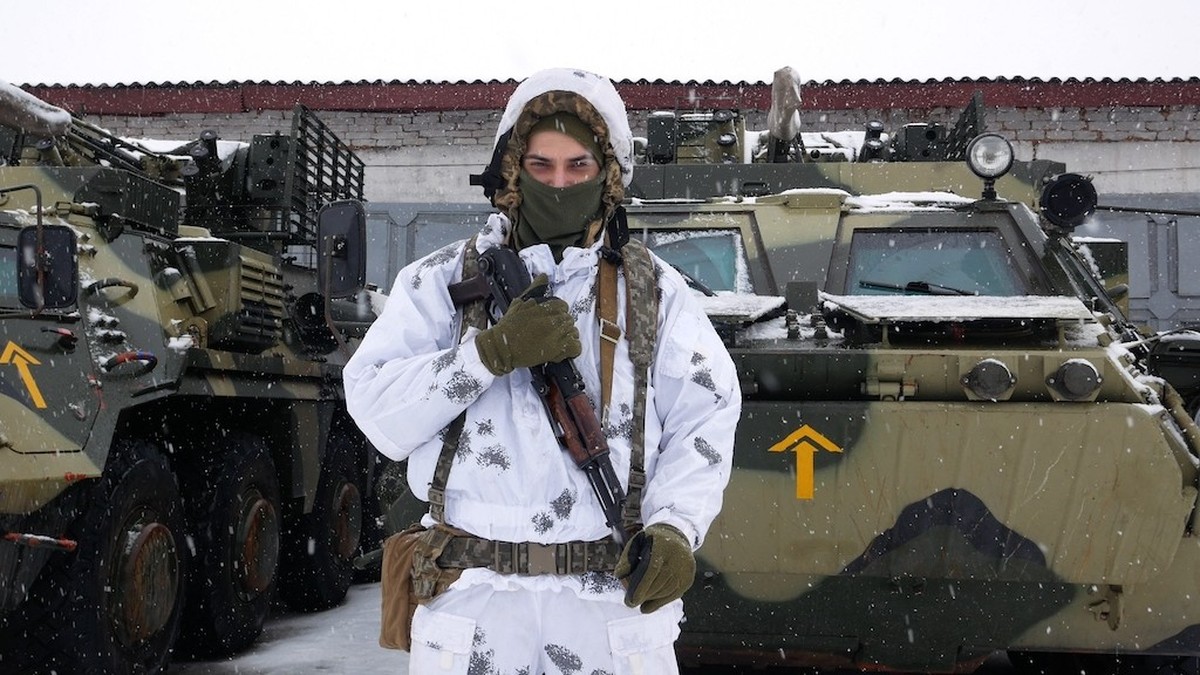 Kharkiv, Ukraine - January, 31, 2022: A soldier in white camouflage with a machine gun stands near armored personnel carriers. The Ukrainian army is preparing to repel the attack of Russia