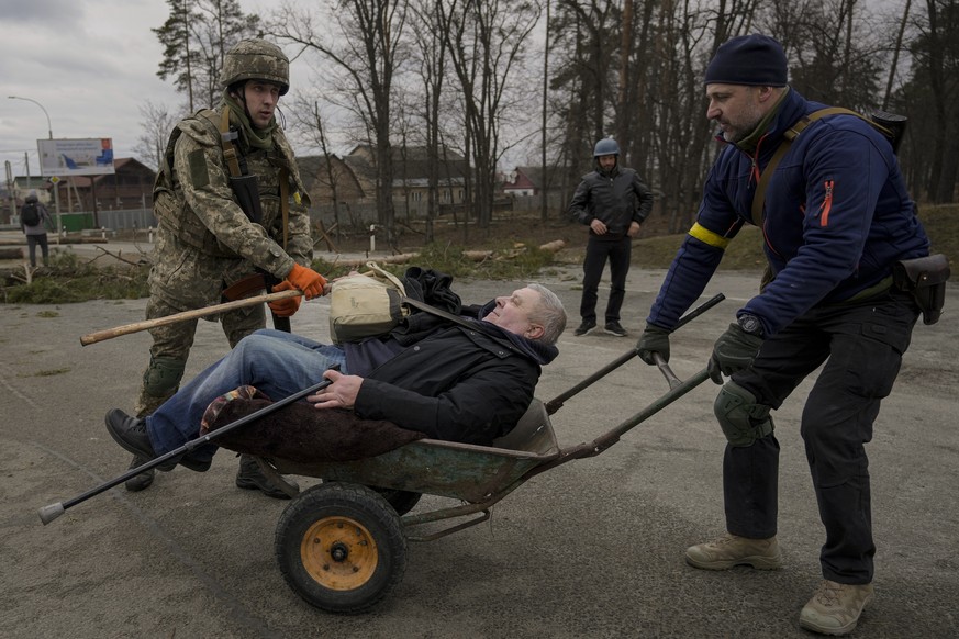 A man is helped in a wheelbarrow after crossing on an improvised path under a bridge that was destroyed by a Russian airstrike, as people flee the town of Irpin, Ukraine, Saturday, March 5, 2022. What ...