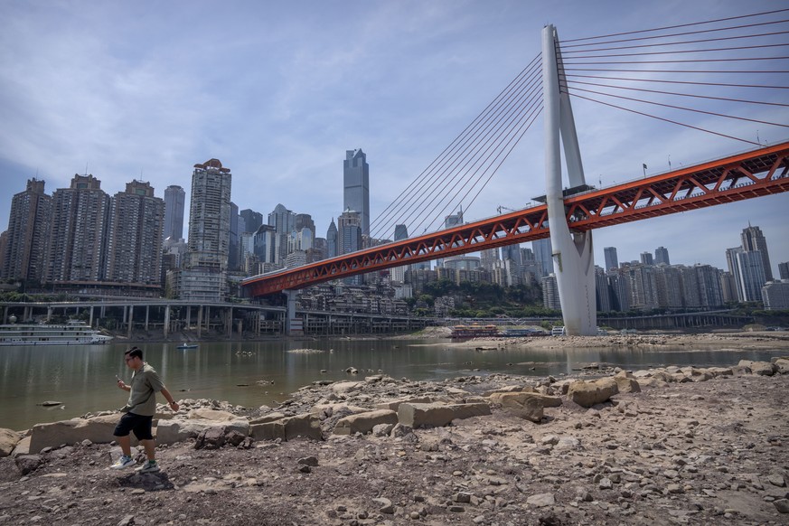 A man walks along the lower than normal bank of the Jialing River in southwestern China&#039;s Chongqing Municipality, Friday, Aug. 19, 2022. Ships crept down the middle of the Yangtze on Friday after ...