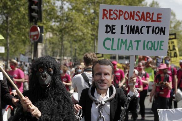 A protester wearing a mask depicting French President Emmanuel Macron holds a bord reading «� Liable for climate inaction� » during a rally against the climate change in Paris, Sunday, May 9, 2021. Th ...