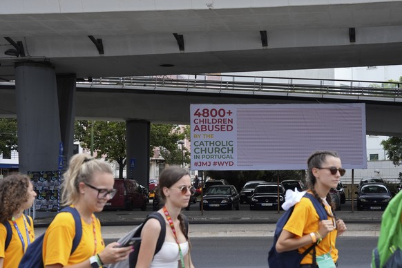 World Youth Day pilgrims walk by a protest billboard against alleged child abuse by the catholic church in Alges, just outside Lisbon, Wednesday, Aug. 2, 2023. Pope Francis has started his five-day pa ...