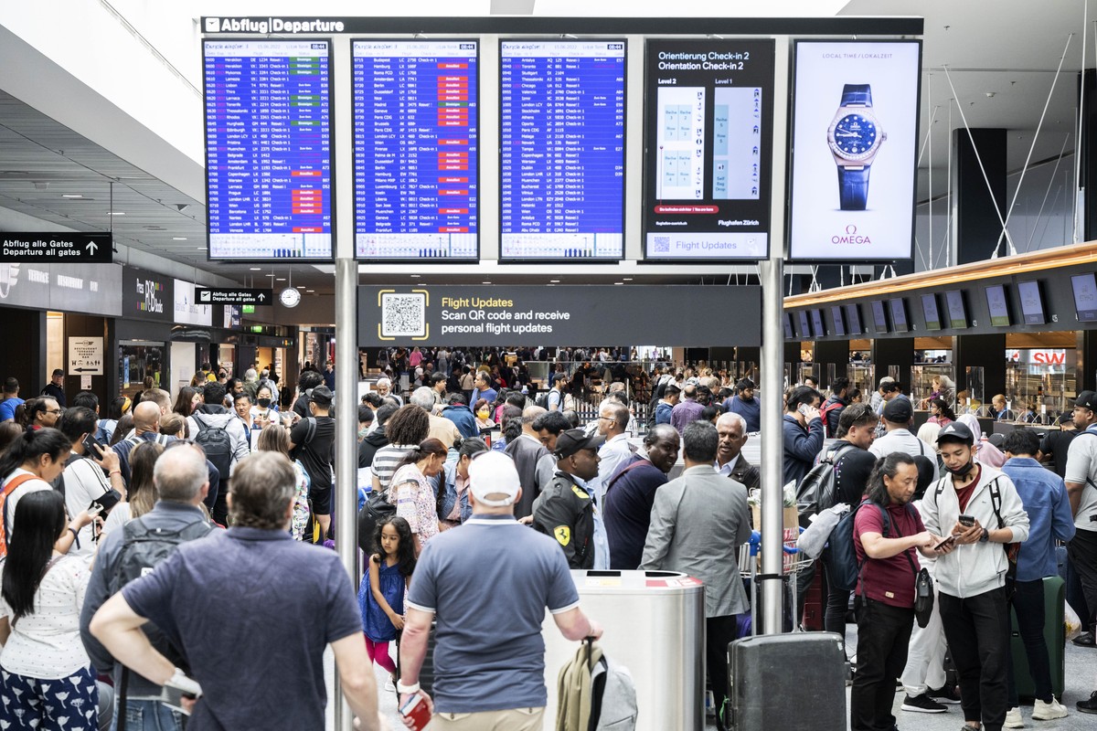Passengers wait in front of a display board at Zurich airport, in Zurich, Wednesday, June 15, 2022. Switzerland