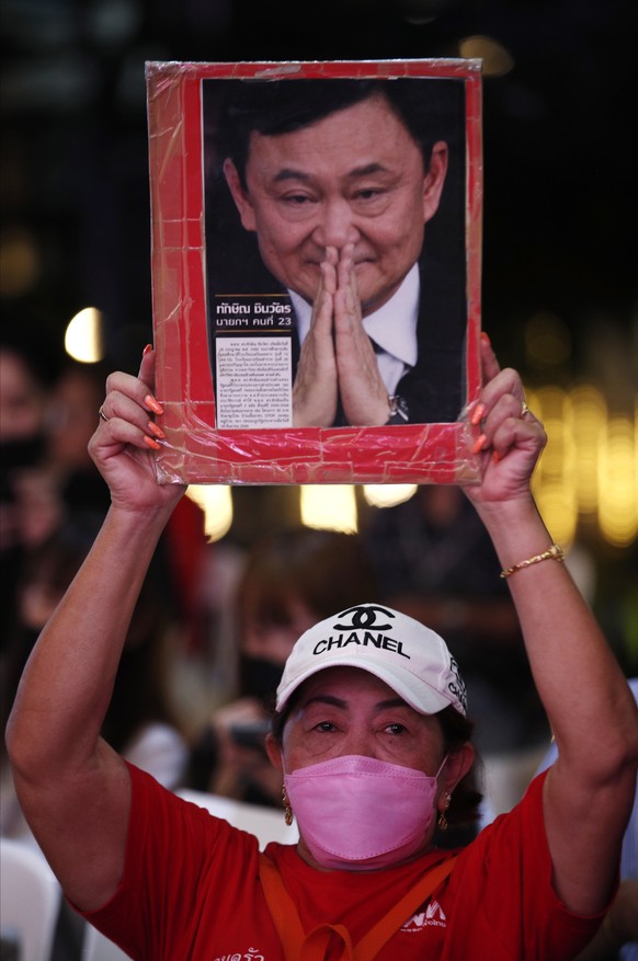 epa10627316 A supporter of Pheu Thai Party holds up a portrait of the former prime minister and founder of the party, Thaksin Shinawatra, while watching a television broadcast of the election vote cou ...