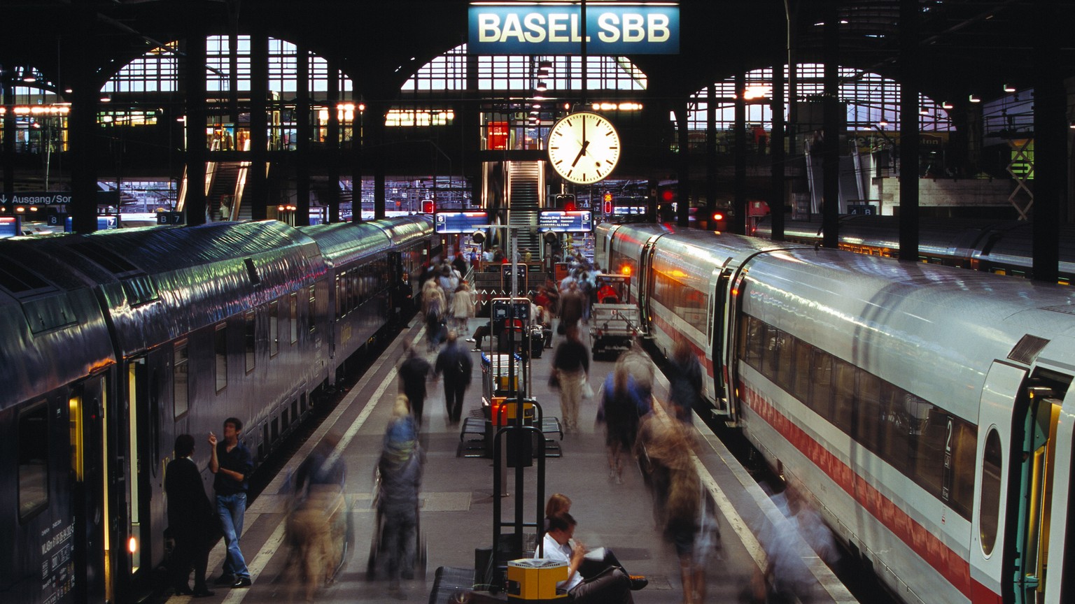 ZUM 75-JAEHRIGEN JUBILAEUM DER SBB BAHNHOFUHR (1944) STELLEN WIR IHNEN FOLGENES BILDMATERIAL ZUR VERFUEGUNG --- Auf dem Bahnsteig im Bahnhof Basel sind Reisende in der Abenddaemmerung auf dem Weg zu i ...