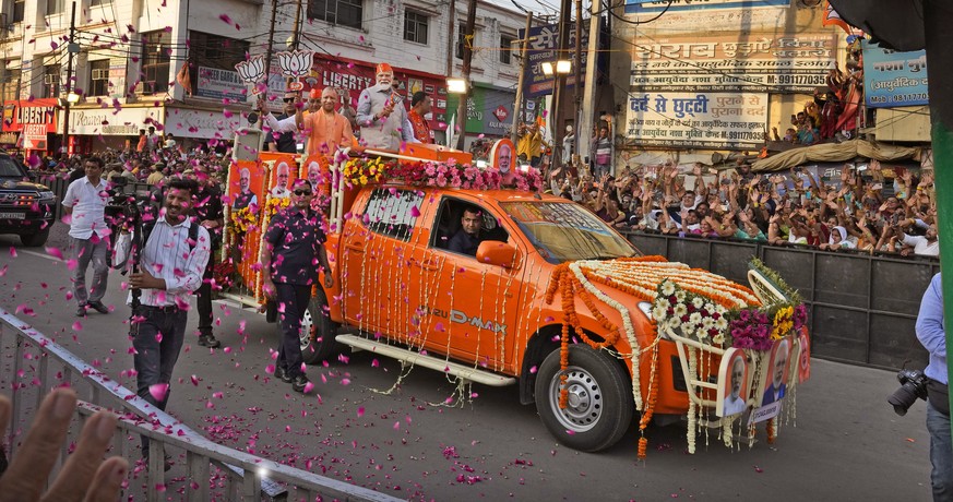 Indian Prime Minister Narendra Modi, center in a saffron cap, and Chief Minister of Uttar Pradesh Yogi Adityanath, in saffron robes, ride in an open vehicle as they campaign for Bharatiya Janata Party ...