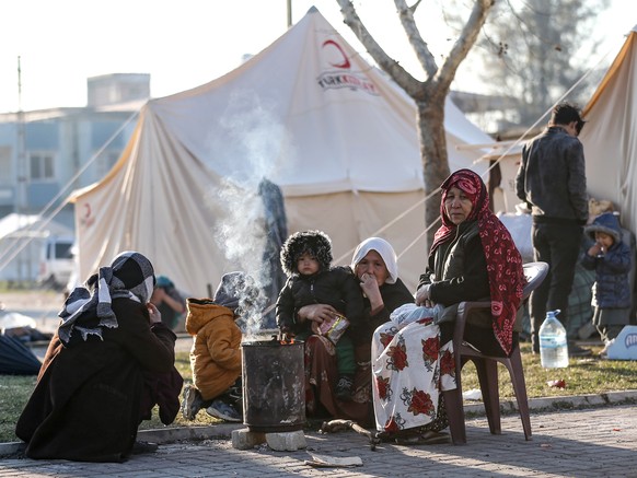 epa10456439 People sit outside a tent following a major earthquake in Hatay, Turkey, 09 February 2023. More than 17,000 people have died and thousands more injured after two major earthquakes struck s ...