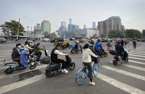 People riding scooters and bicycles wait at an intersection in the central business district in Beijing, Wednesday, Oct. 12, 2022. A meeting of the ruling Communist Party to install leaders gives Pres ...