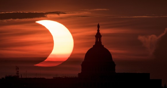 epa09259307 A handout picture made available by the National Aeronautics and Space Administration (NASA) shows a partial solar eclipse as the sun rises to the left of the United States Capitol Buildin ...