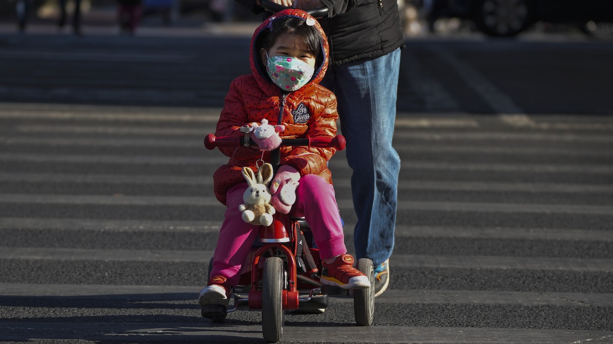 A woman pushes a child on a bicycle as they cross a street in Beijing, Wednesday, Jan. 4, 2023. The Chinese government sharply criticized COVID-19 testing requirements imposed on visitors from China a ...