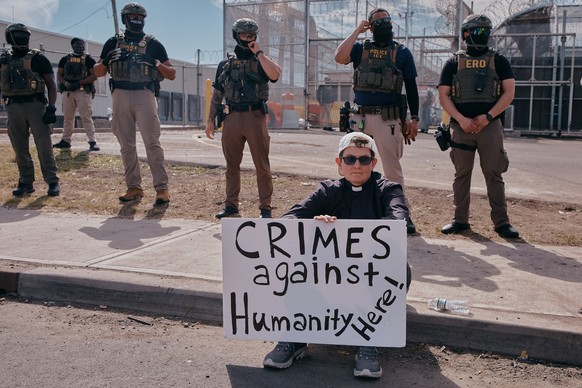 A protester holds a sign as ICE agents stand guard outside the Delaney Hall detention during a protest against the transfer of detainees on Tuesday, May 26, 2026, in Newark, N.J. (AP Photo/Andres Kuda ...