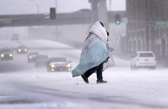 A person wrapped in a blanket crosses a snow-covered street Thursday, Dec. 22, 2022, in St. Louis. The frigid air is moving through the central United States to the east, with windchill advisories aff ...